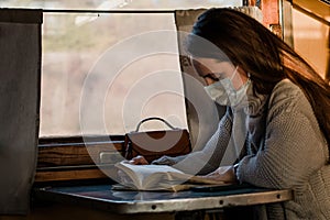 A young woman is traveling by train during coronavirus pandemic and reading