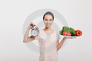 young woman with tray of various fresh vegetables and alarm clock
