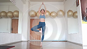 Young woman in tree pose doing yoga in the gym in sportswear. The concept of stretching, pilates, yoga. Vrikshasana.