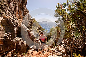 young woman with trekking poles in her hands climb up the rocky trail