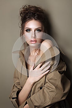 Young woman in trench cout with evening make up and hairdo