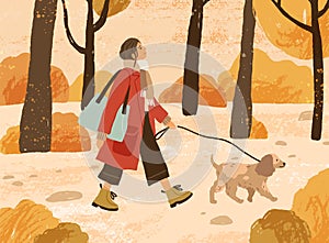 Young woman in trendy warm outwear walking dog in autumn park, admiring nature. Fashionable female character with pet in