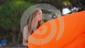 Young woman on a tropical beach inflate an inflatable sofa. Summer vacation concept