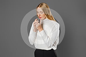 Young woman in trousers and sweater holds cup of coffee with both hands