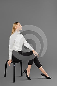 Young woman in trousers and sweater sits in profile in studio