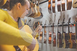 Young woman trying, buying new guitar in a instrument shop, instrumental concept
