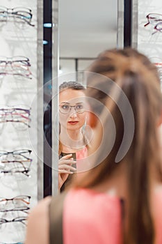 Young woman trying fashionable glasses in optometrist store