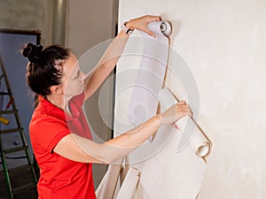 Young woman trying out new wallpaper at home holding the roll up against a newly painted white wall for visual effect