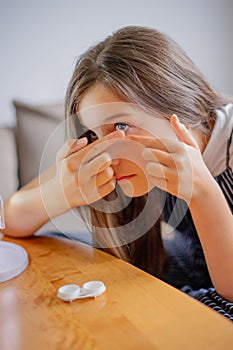 Young woman trying to apply contact lenses in front of mirror. Young girl trying on new contact lenses. Close up of girl trying on