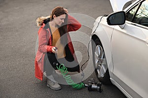 Young woman trying to inflate car tire with air compressor on street