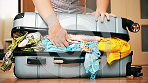 Young woman trying to pack overfilled suitcase