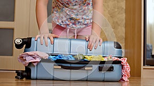 Young woman trying to pack overfilled suitcase