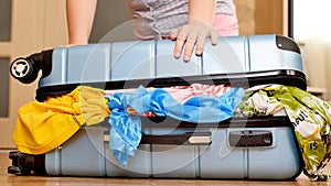 Young woman trying to pack overfilled suitcase