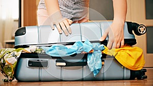 Young woman trying to pack overfilled suitcase