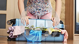 Young woman trying to pack overfilled suitcase