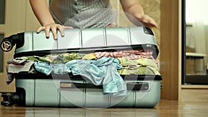 Young woman trying to pack overfilled suitcase