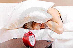 Young woman trying to sleep when alarm clock ringing