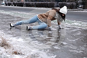 Young woman trying to stand up after falling on slippery icy pavement outdoors