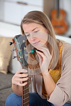 young woman tuning acoustic guitar