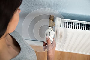 Young woman turning thermostat on radiator