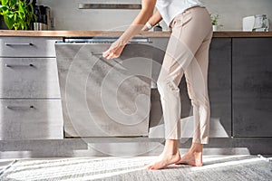 Young woman turns on the dishwasher by pressing buttons on the panel. Household and useful technology concept.