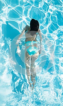 Young woman in turquoise bikini swimming under water in a swimming pool