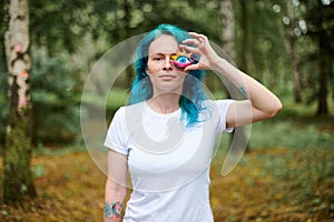 Young woman with turquoise dyed hair in white T shirt holds handmade colorful eye talisman