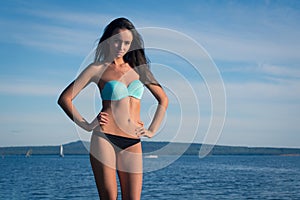 Young woman in a turquoise swimsuit near the water sunbathing on the beach