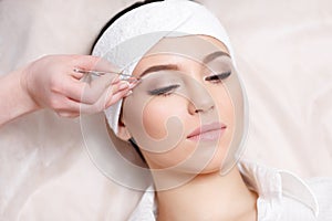 Young woman tweezing her eyebrows in beauty saloon