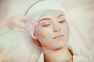 Young woman tweezing her eyebrows in beauty saloon