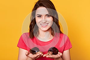 Young woman with two giant Achatina snails stands over yellow background, wears pink casual t shirt, posing with toothy smile,