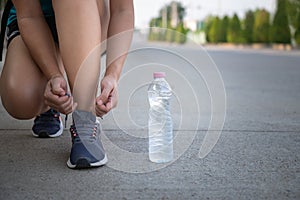 Young woman tying laces with drinking water bottle