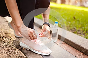 Young woman tying laces on her sneakers in summer park at sunset. Runner having rest. Sport concept.