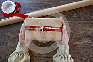 Young woman tying ribbon on gift box on wooden background