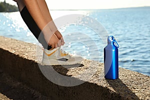 Young woman tying shoelaces near bottle