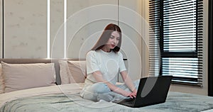 Young woman typing on laptop. Girl typing messages on laptop chatting with friends sitting in bed at home. Female person