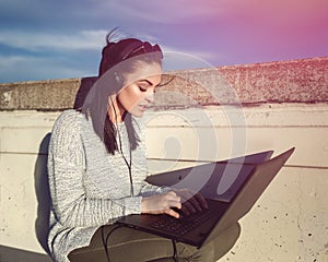 Young woman typing on laptop and listening music outdoor