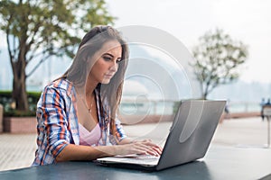 Young woman typing on a laptop studying or working in the park