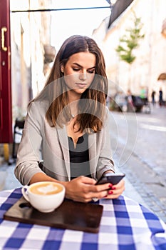 Young woman typing text message on smart phone in a cafe. Young woman sitting at a table with a coffee using mobile phone