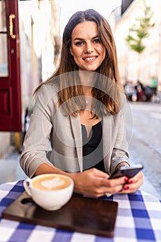 Young woman typing text message on smart phone in a cafe. Young woman sitting at a table with a coffee using mobile phone