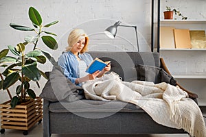 Young woman under a blanket reading book on couch