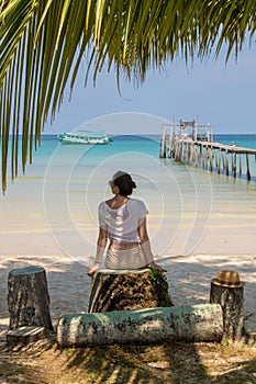 A young woman under a palm tree on the shore of the Gulf of Thailand. Woman in a hat looks at the sea