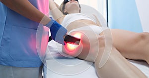 Young woman undergoes procedure for laser hair removal of legs in beauty salon