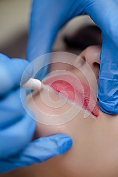 Young woman undergoing procedure of permanent lip makeup in tattoo salon, closeup