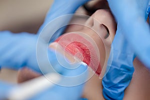 Young woman undergoing procedure of permanent lip makeup in tattoo salon, closeup