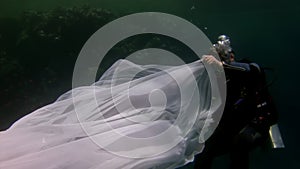 Young woman underwater model in white cloth on background of blue water.