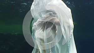 Young woman underwater model in white cloth on background of blue water.