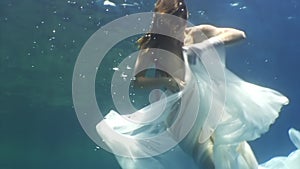 Young woman underwater model in white cloth on background of blue water.