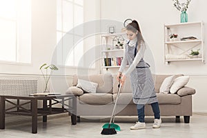 Young woman sweeping house with broom and scoop