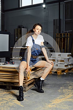 Young woman in uniform sits on a stack of chipboard slabs